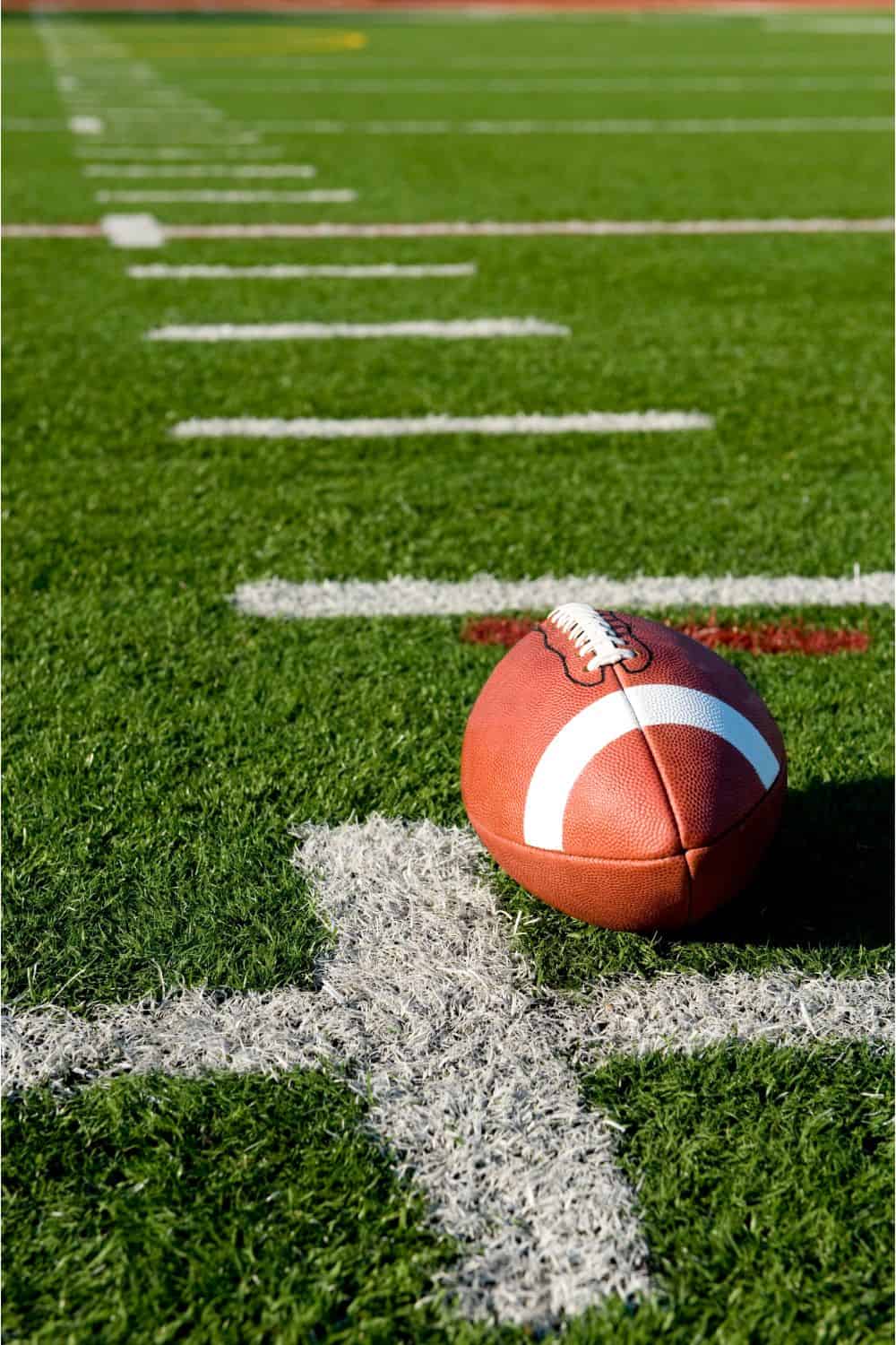 A football resting on a green field, perfectly placed on a white yard line, under the clear sky in Goodyear AZ, showcases the precision of an expert artificial grass installer.